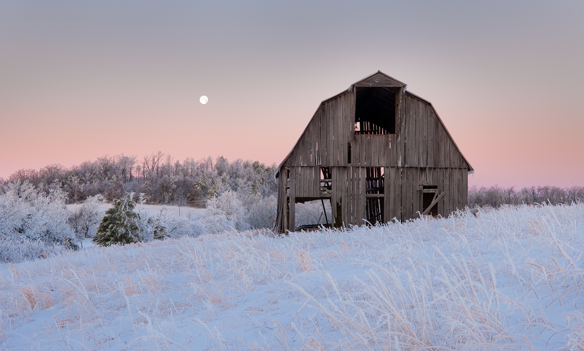 A full moon sets on the horizon behind this old barn, which has since fallen and been removed.